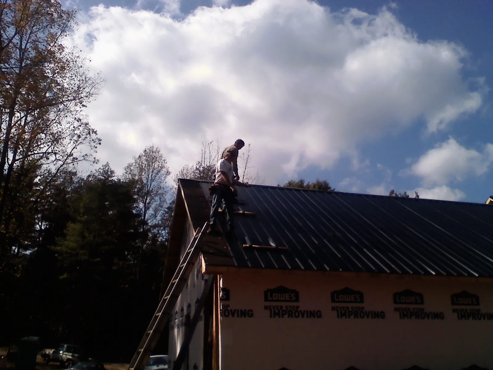 Roofer fastening dark metal panels high against a cloudy sky, from a Roof Inspection job in Carlisle